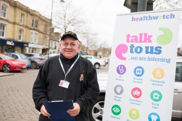 Man standing infront of a Healthwatch Talk to Us sign at a community event