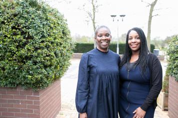 Two women stood in a courtyard with their arms round each other