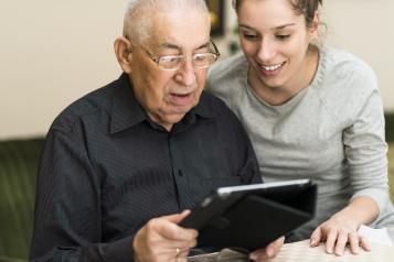 Image of young woman helping an elderly man with a tablet