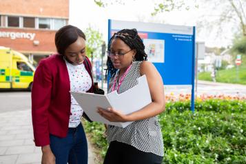 Two women standing outside a hospital looking at a document