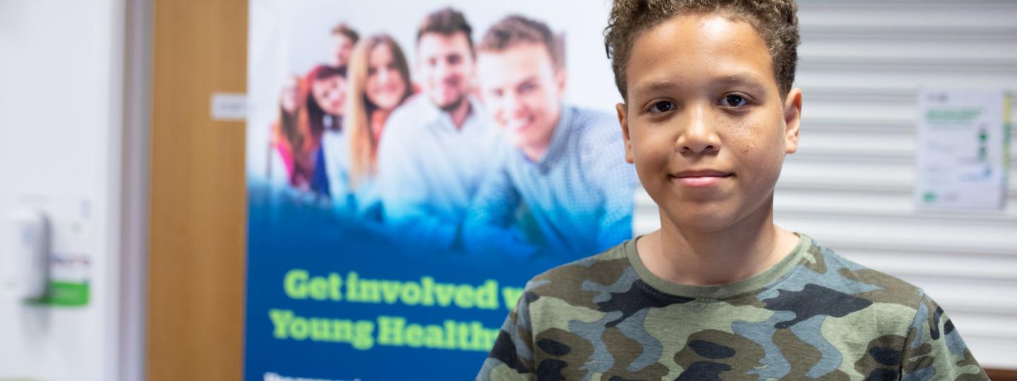 Young boy standing in front of a Healthwatch poster