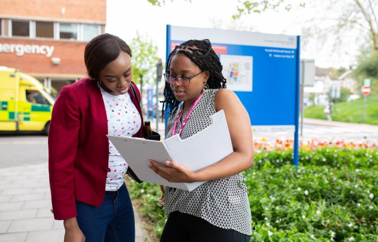 Two women standing outside a hospital looking at a document